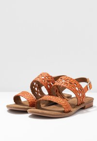 Woven orange leather sandals with an open toe, adjustable ankle strap, and a flat sole, featuring a textured, soft footbed.