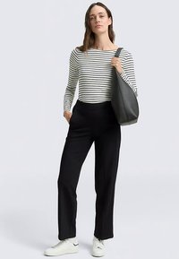 Haut à manches longues rayé en noir et blanc, accompagné d'un pantalon noir ample et de baskets blanches. Le modèle porte un sac à bandoulière gris foncé.