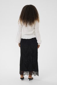 Fehér fodros hosszú ujjú felső, dús ujjakkal, fekete csipkés maxi szoknyával, mely virágmintás és hullámos szegéllyel rendelkezik.