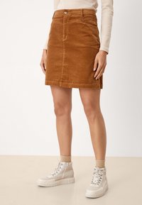 Jupe en velours côtelé marron avec poches avant, de forme structurée, bouton centré, longueur au-dessus du genou, associée à des bottines claires.