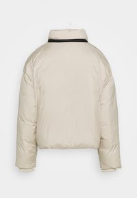 Giacca puffer cropped beige con collo alto, finitura opaca e polsini a costine. Il design include un accento nero sullo scollo.