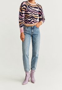Suéter de punto con rayas de tigre en rosa, beige y azul marino; jeans de mezclilla azul claro; botas de tobillo de encaje lavanda; corte relajado, textura suave.