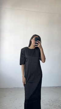 Vestido negro con una silueta recta, mangas cortas abullonadas y cuello redondo. Textura suave, cuenta con detalles en panel y largo hasta el tobillo.