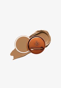 Bronse kompakt med en blank overflate og preget logo, som rommer kremfundament. Brun fargeprøve av fundamentet ligger ved siden av kompakt.
