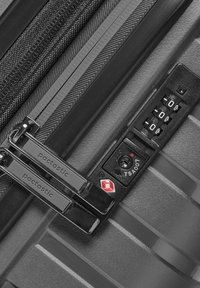 Valise rigide noire avec une surface texturée, deux zippers, une serrure à combinaison et un cadenas de sécurité approuvé par la TSA arborant un emblème rouge.