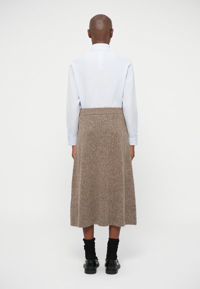 Ανοιχτού μπλε πουκάμισο με κολάρο με κουμπιά, συνδυασμένο με φούστα καφέ, υφή μέχρι το γόνατο και μαύρες κάλτσες και παπούτσια μέχρι τον αστράγαλο.