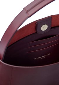 Innenraum der burgunderfarbenen Ledertasche mit glatter Textur, Druckverschluss und mehreren Kartenfächern. Sichtbares Logo in Goldfolie.