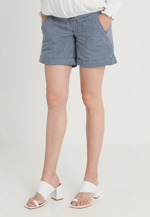 Bermudas a rayas en azul marino y blanco con un corte relajado, bolsillos laterales y dobladillo doblado. Combinadas con tacones abiertos blancos.