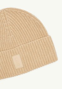 Beżowa dziana czapka beanie z prążkowaną teksturą, z kwadratową skórzaną naszywką z logo na złożonym mankiecie.