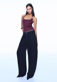 Top bordo cu bretele halter, cu textură lucioasă, asortat cu pantaloni negri supradimensionați, cu croială dreaptă și deschidere largă la picior.