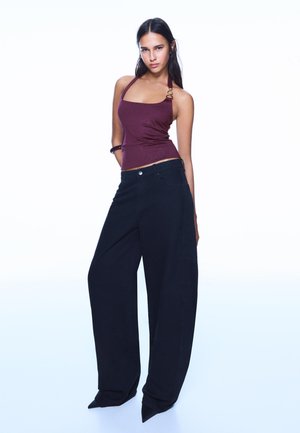 Bordeaux haltertop met glanzende textuur, gecombineerd met oversized zwarte broek met rechte snit en een brede pijpopening.