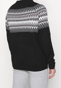 Černý pletený svetr s bílým a šedým geometrickým vzorem na horní části zad a ramenou. Hladké manžety a spodní lem.