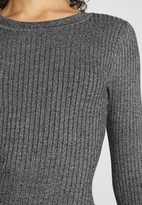 Pull en maille grise à côtes, avec un col rond et des manches longues, présentant un tissu texturé et des rayures verticales sur l'ensemble.