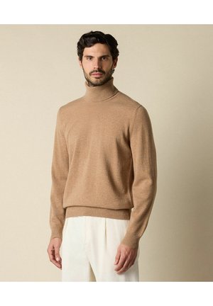 Maglione beige a collo alto in morbido materiale, caratterizzato da un design aderente e dettagli a coste sul colletto e sull'orlo. Abbinato a pantaloni bianchi texturizzati.