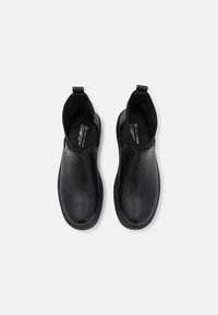 Bottines en cuir noir avec des bouts ronds, des panneaux latéraux élastiques et des languettes pour un enfilage facile. Texture lisse et design minimaliste.