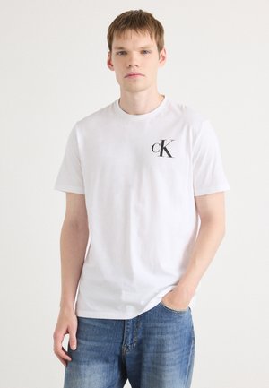 Bela bombažna majica s krožnim izrezom in kratkimi rokavi, na levi strani prsnega dela z črnim logotipom "cK". Ohlapen kroj.