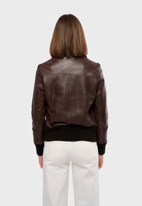 Braune Lederbomberjacke mit gerippten schwarzen Bündchen und Saum. Glatte Oberfläche mit taillierter Silhouette, von hinten betrachtet.