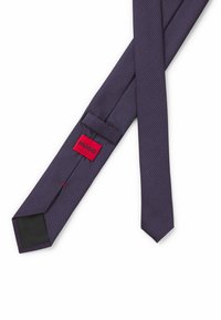Purple tie with a geometric pattern in red and blue. Features a black fabric tip and a red label with "HUGO" text. Smooth texture.