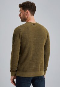 Suéter de punto color verde oliva con puños y dobladillo acanalados, tejido texturizado y detalle de parche lateral. Cuello redondo y corte relajado.