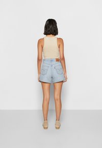 Pantalones cortos de mezclilla azul claro con cintura alta, dobladillos deshilachados y bolsillos traseros que presentan una etiqueta roja desvaída y un diseño de costura ondulada.