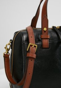 Sort skindtaske med brune detaljer, guldbeslag, lynlås lukning og to håndtag. Har en aftagelig skulderrem med spænde.