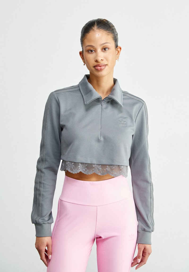 Grå cropped sweatshirt med krage, blondekant og ribbestrikkede mansjetter; kombinert med rosa tettsittende leggings med subtil merkevare.