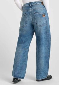 Jean en denim bleu clair à jambes larges avec une finition délavée. Comprend des poches arrière et une étiquette en cuir marron sur la taille arrière.