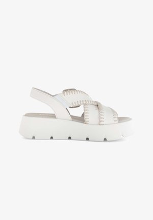 Witte platform sandaal met dikke geribbelde zool, gevlochten kruisbanden en verstelbare achterband, weergegeven tegen een witte achtergrond.