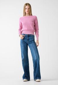Pink ribbed knit sweater paired with high-waisted flared blue denim jeans, featuring visible stitching and a relaxed fit.