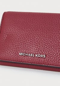 Portafoglio in pelle testurizzata bordeaux con logo argento "MICHAEL KORS". Design compatto con dettagli di cuciture.