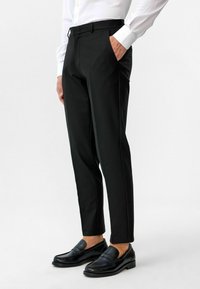 Zwarte op maat gemaakte broek met een slim fit, voorzien van voorzakken en een gladde textuur; gecombineerd met zwarte instappers.