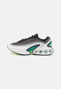 Fekete és fehér hálós felsőrészes Nike sportcipők zöld részletekkel, és tapintásos talppal, amely átlátszó légpárnákkal rendelkezik a párnázás érdekében.