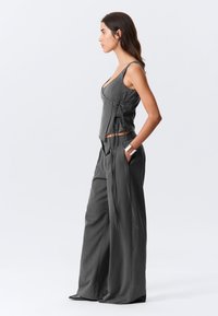 Tenue grise en deux pièces comprenant un haut ajusté avec des cordons réglables et un pantalon à jambes larges. Le tissu présente une texture subtile à fines rayures.