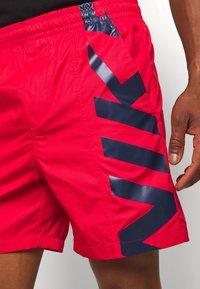 Un maillot de bain rouge fabriqué dans un matériau léger présente de grands accents graphiques bleu marine sur le côté. Taille élastique pour un ajustement réglable.