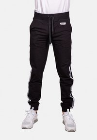 Svarta joggers med elastiskt midjeband och dragsko. Vita sidosträck har varumärket tryckt. Slät tygkvalitet med avsmalnande ben.