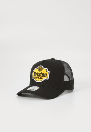 Black trucker hat with mesh sides, featuring a yellow and black embroidered BRIxton logo on the front. Curved brim and adjustable strap.