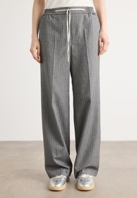 Pantalons gris à rayures avec une taille élastique et un cordon de serrage. Coupe ample et tissu texturé. Associés à des baskets argentées.