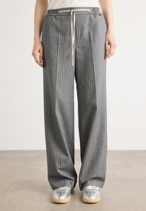 Pantalons gris à rayures avec une taille élastique et un cordon de serrage. Coupe ample et tissu texturé. Associés à des baskets argentées.