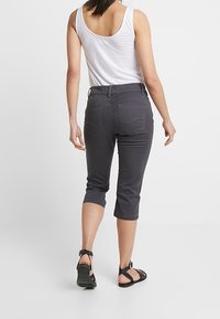 Pantalons cropped gris en denim, avec une coupe ajustée, des poches à l'arrière et un ourlet retroussé, associés à un débardeur blanc et des sandales.