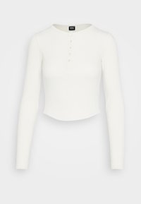 Vit långärmad cropped topp i ribbat tyg, med rund halsringning och sex knappar längs framtill.