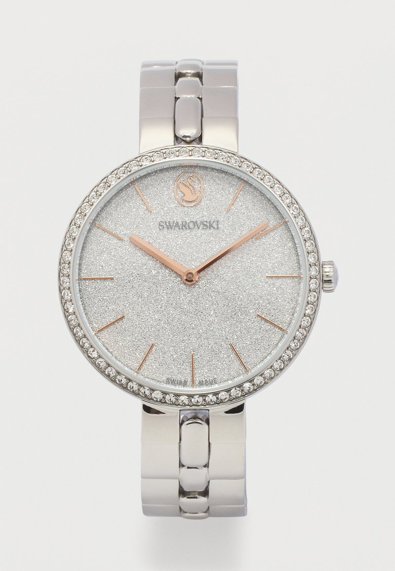 Ασημένιο ρολόι Swarovski με στεφάνι καλυμμένο με κρύσταλλα, λαμπερό καντράν, δείκτες και σημεία ώρας σε ρόζ χρυσό, και μπρασελέ με μεταλλικούς κρίκους.