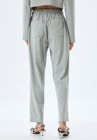 Hellgraue maßgeschneiderte Hose mit einem elastischen Bund, zwei Gesäßtaschen und schmal zulaufendem Schnitt. Hergestellt aus einem strukturierten Stoff.