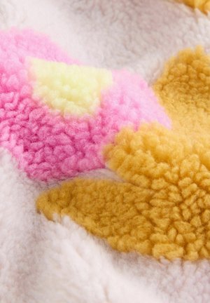 Textuurstof in zachte roze, gele en beige tinten, met pluche bloemmotieven. Het materiaal lijkt vezelig en dik, met duidelijke kleursecties.