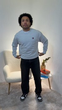 Γκρι φούτερ με μακριά μανίκια, λογότυπο στο στήθος, σε συνδυασμό με μαύρο παντελόνι και αθλητικά παπούτσια. Στο φόντο εμφανίζεται μια λευκή καρέκλα και βιβλία.