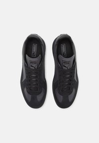 Black athletic shoes with suede and synthetic panels, featuring a textured sole, lace-up design, and subtle logo accents on the tongue.