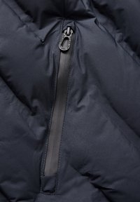 Gros plan sur un tissu de veste rembourrée bleu marine, mettant en avant une fermeture éclair étanche et une texture lisse avec un motif de matelassage géométrique.