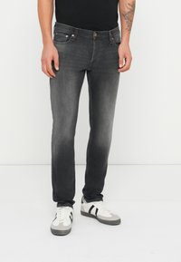 Jeans de denim gris oscuro con un corte ajustado, diseño de cinco bolsillos, ligero desgaste y costuras en contraste. Combinados con zapatillas blancas.