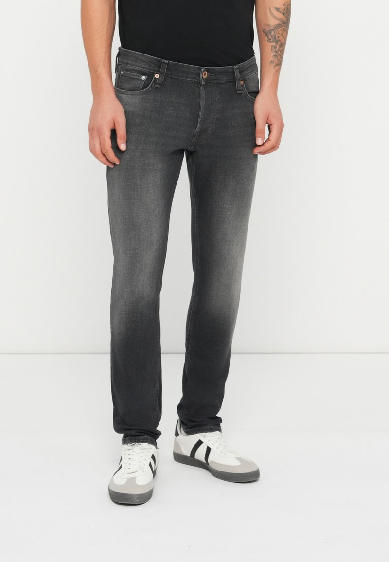 Jeans de denim gris oscuro con un corte ajustado, diseño de cinco bolsillos, ligero desgaste y costuras en contraste. Combinados con zapatillas blancas.