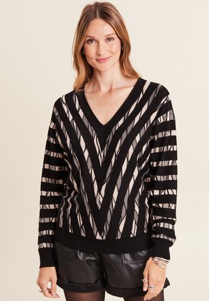 Black and beige V-neck sweater featuring vertical and horizontal stripes, textured fabric, and ribbed cuffs and hem, paired with black shorts.