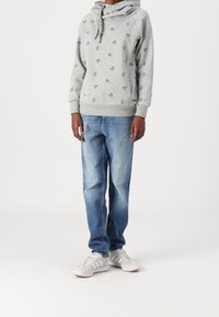 Szara bluza z kapturem z czarnym kwiatowym nadrukiem, wyposażona w ściągacz na kaptur, ściągacze na mankietach i u dołu, zestawiona z jasnoniebieskimi prostymi dżinsami i białymi trampkami.